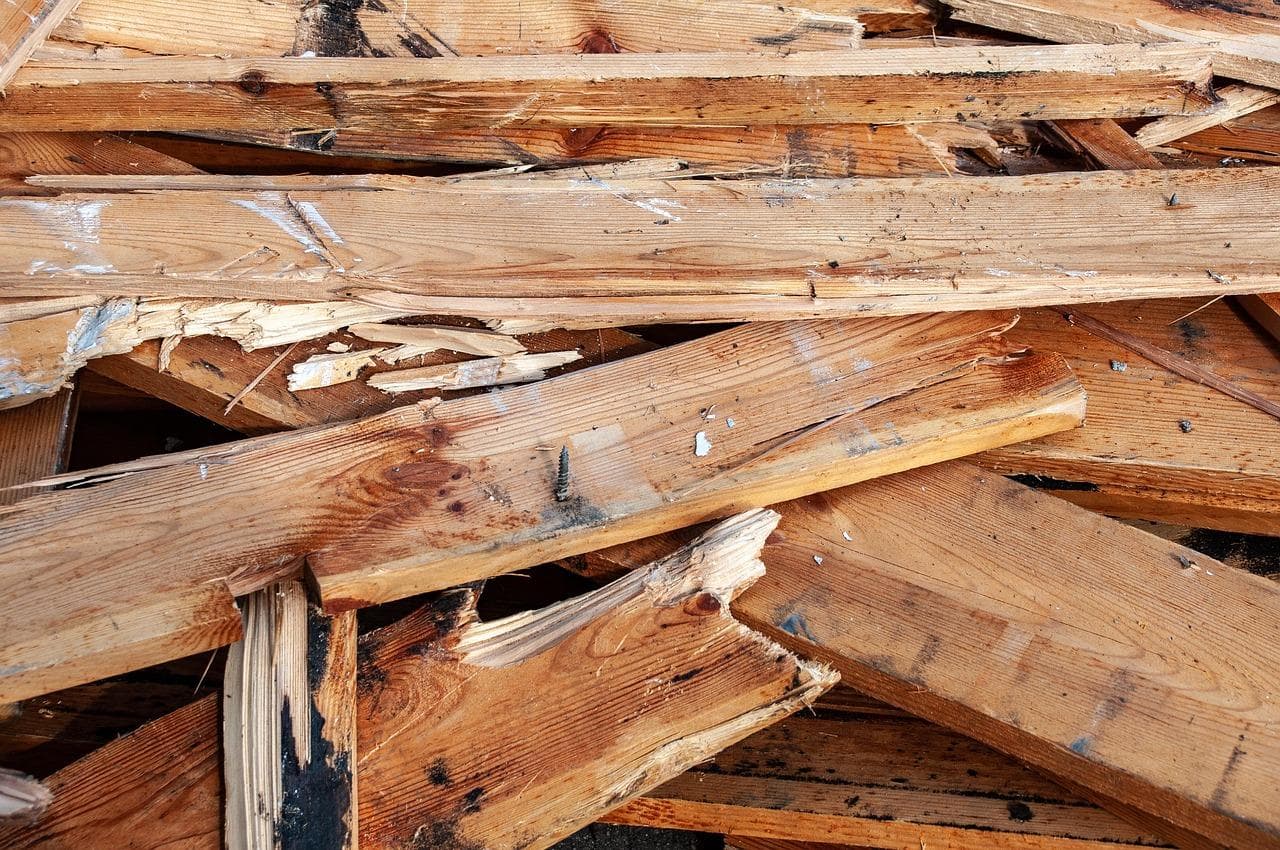 A pile of broken, splintered wooden boards stacked haphazardly, with visible nails, cracks, and dark stains on the wood surfaces.