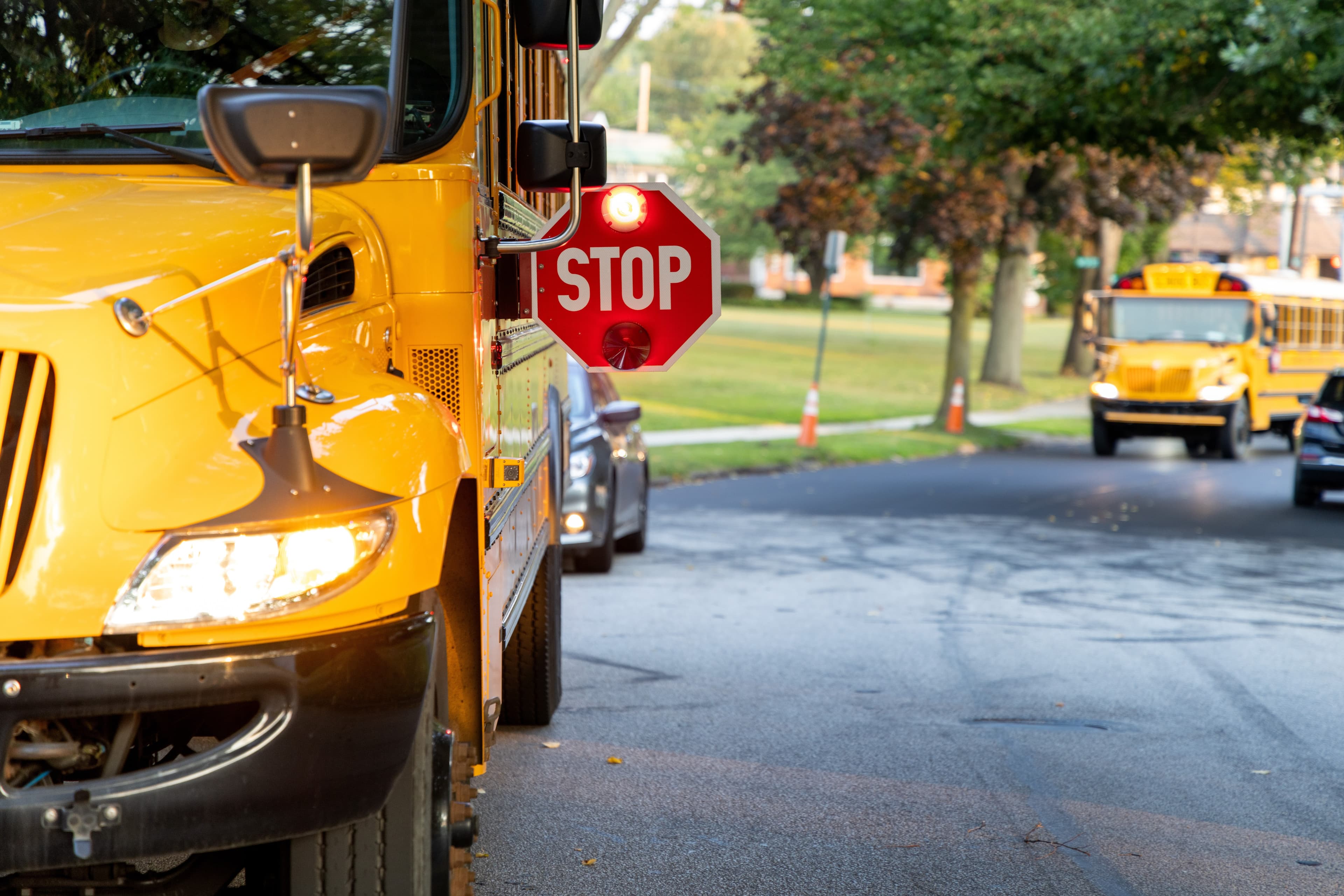 Yellow school bus stopped with its red stop arm extended on a tree-lined residential street