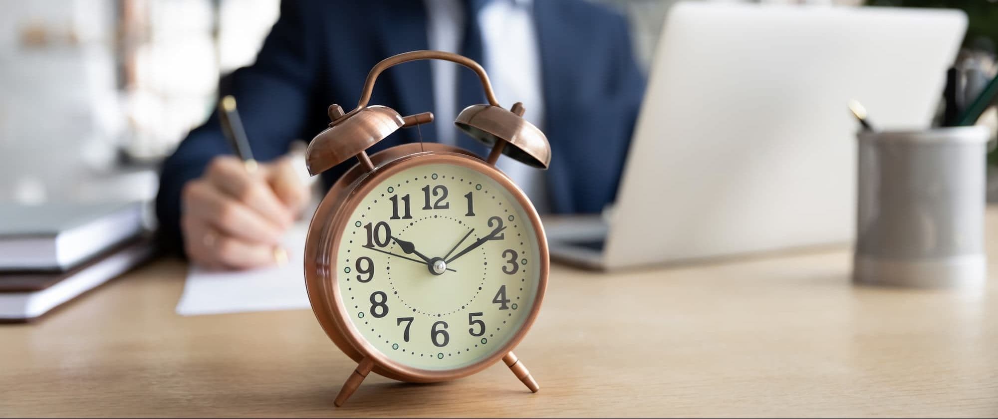 Clock in the foreground. Lawyer holding a pen over a piece of paper on the same table in the background | Personal Injury | The Sullivan Law Firm