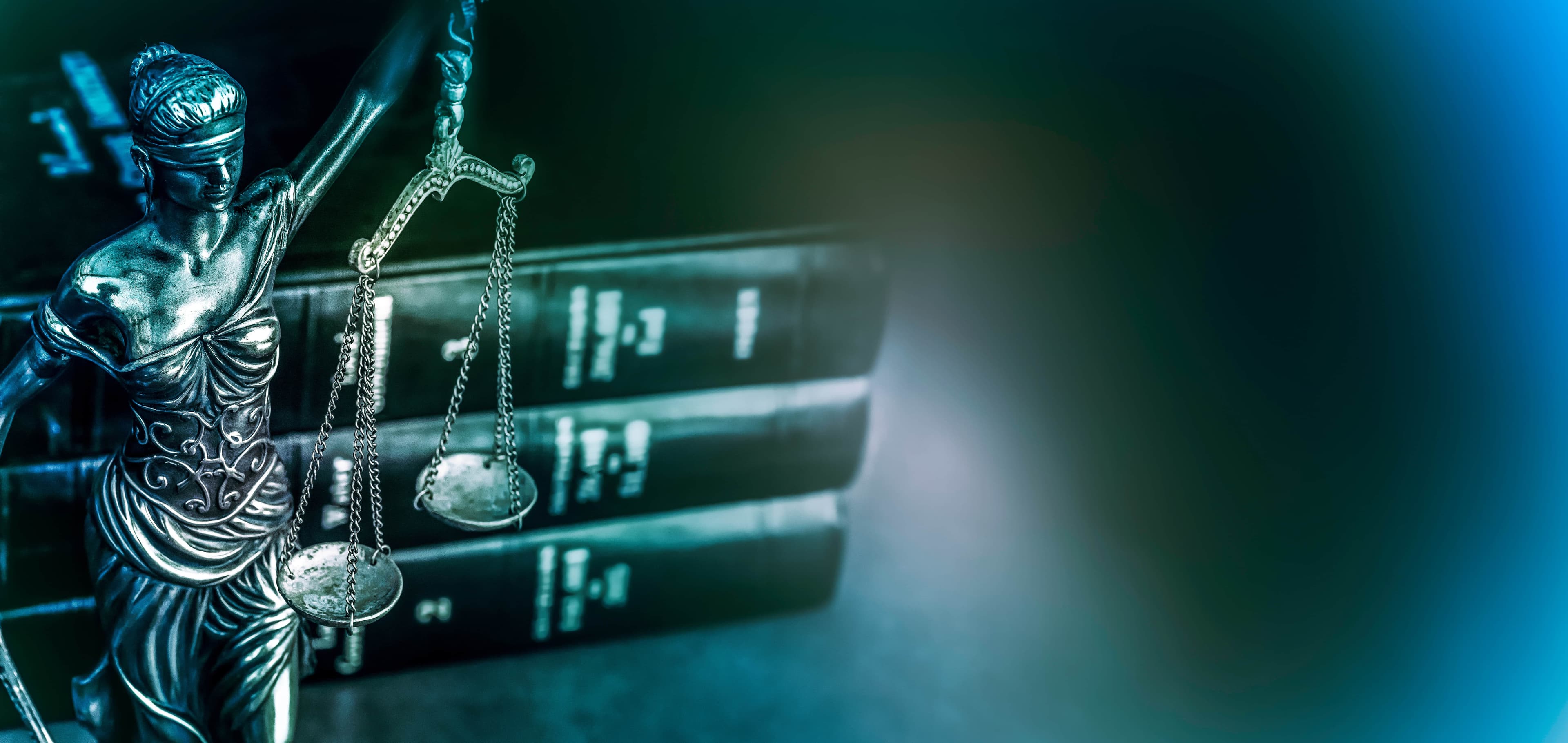 Black and white image of a small statue of Lady Justice holding her balance and wearing a blindfold in front od a stack of law books | Unleashing Justice | The Sullivan Law Firm
