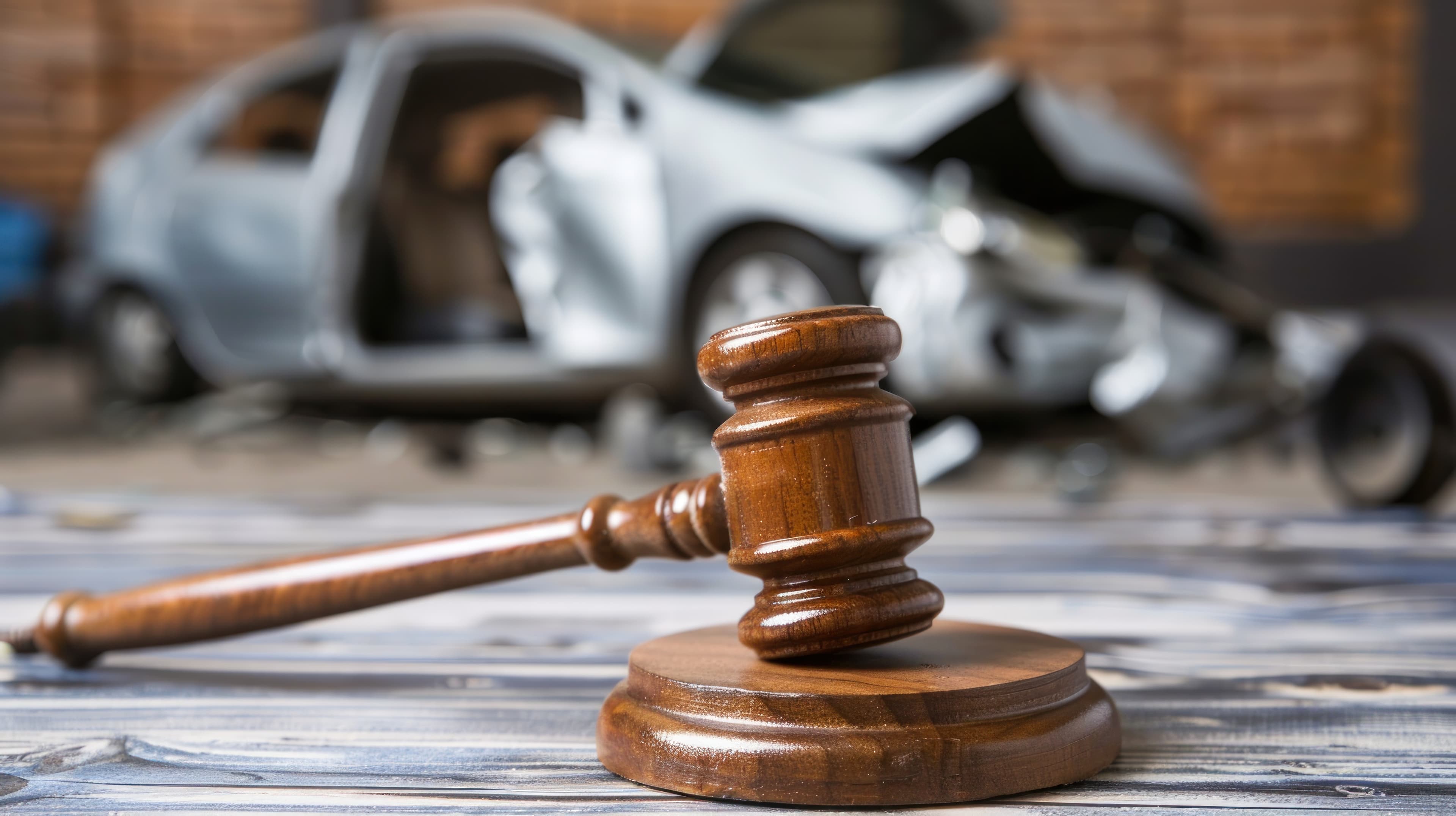 Wooden gavel in foreground. Wrecked car in the background | Personal Injury | The Sullivan Law Firm